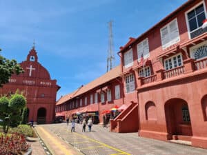 Colorful Melaka Christ Church and historic red Dutch square in Melaka, Malaysia, with tourists enjoying the vibrant street scene and shops, showcasing Melaka’s rich cultural heritage and colonial architecture.