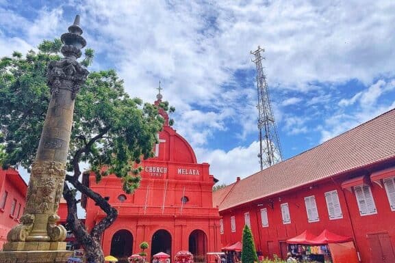 Colorful heritage church in Melaka, Malaysia, with historic architecture and vibrant red exterior, surrounded by lush trees and sky, showcasing Melaka’s rich cultural history and colonial influence.