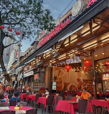 Vibrant outdoor dining scene at Onalulu restaurant with red tablecloths, Chinese lanterns, and bustling atmosphere in an urban Chinatown setting, attracting locals and tourists.