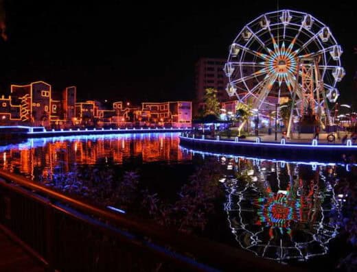 Onalulu 游乐园里，夜晚灯光璀璨的摩天轮倒映在水面上，与绚丽的城市灯光交相辉映，营造出浓厚的节日氛围，是夜间观光和娱乐的理想场所。.