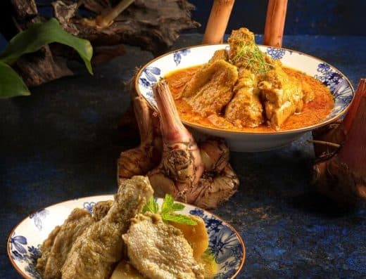 正宗印尼美食，包括香辣浓郁的仁当鸡和酥脆的炸鱼，盛放在传统的蓝白花纹碗中。是美食爱好者品尝正宗印尼菜肴的理想之选。.