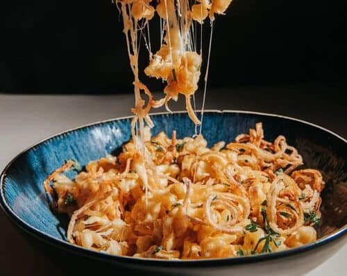 Delicious seafood and cheese pasta in a black bowl, with melted cheese stretching. Fresh herbs garnish for added flavor, perfect for a savory dining experience.