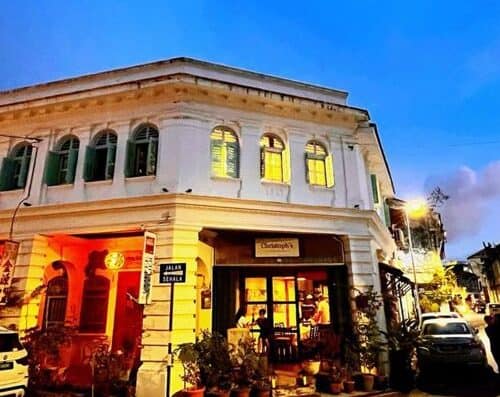 A beautifully illuminated historic building on a scenic street, featuring vintage architecture with large windows, vibrant lighting, and cozy outdoor seating, ideal for dining or relaxing.