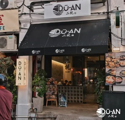 A vibrant street view of Duan restaurant showcasing its stylish black awning and inviting entrance, perfect for authentic Asian cuisine and noodle dishes.
