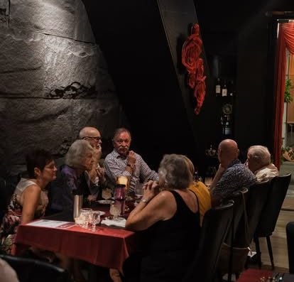 一群成熟的成年人在一家时尚、灯光昏暗的餐厅享用晚餐，桌上摆放着饮料和食物，营造出温馨的社交氛围，非常适合聚会。.