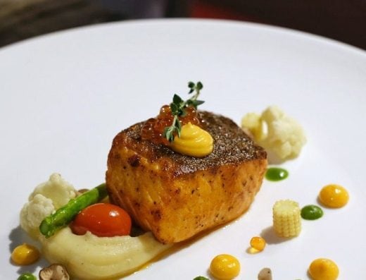 Delicious seared salmon fillet served with mashed potatoes, cherry tomatoes, asparagus, cauliflower, baby corn, and colorful sauces on a white plate.