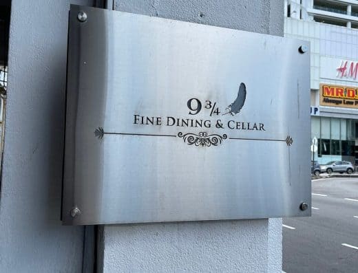 Stylish metallic sign displaying "9 3/4 Fine Dining & Cellar" with feather graphic, mounted on a wall, representing luxury restaurant branding and fine dining experience.