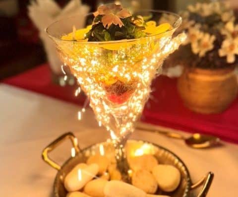 一款华丽的鸡尾酒，盛放在马提尼酒杯中，饰以可食用鲜花、闪亮的烟花和新鲜水果，放在铺有鹅卵石的装饰托盘上，是特殊场合或庆祝活动的完美之选。.