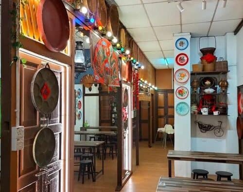 A welcoming Asian restaurant interior featuring decorative plates on the walls, string lights, and cozy dining tables with black chairs.