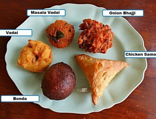 A plate featuring traditional Indian snacks including Vada, Bonda, Masala Vadai, Onion Bhaji, and Chicken Samosa, perfect for tea-time or as appetizers.