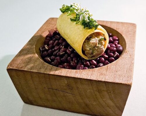 新鲜的墨西哥卷饼，内含豆子，盛于木盘中，并以香草点缀。.