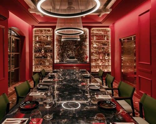 Elegant modern dining space with a sleek black marble table, stylish green chairs, and striking red walls illuminated by artistic lighting fixtures, perfect for upscale gatherings and fine dining experiences.