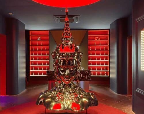 Intricate golden statue of a regal figure with a crown, displayed in a stylish boutique setting with red illuminated shelves in the background. Perfect for luxury art and decor enthusiasts.