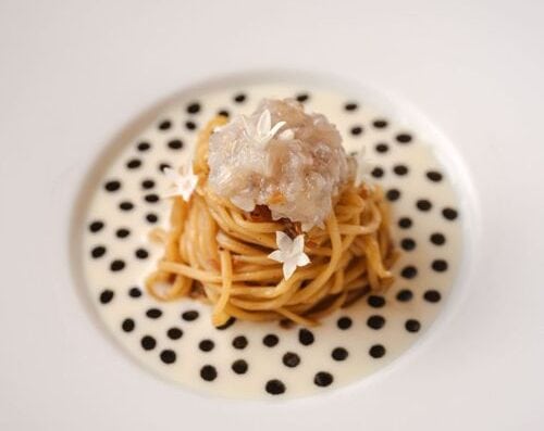 美味的海鲜意面盛放在饰有黑色波点的时尚白色盘子上，上面点缀着可食用的花朵，展现出精致的美食摆盘，是美食爱好者的完美之选。.